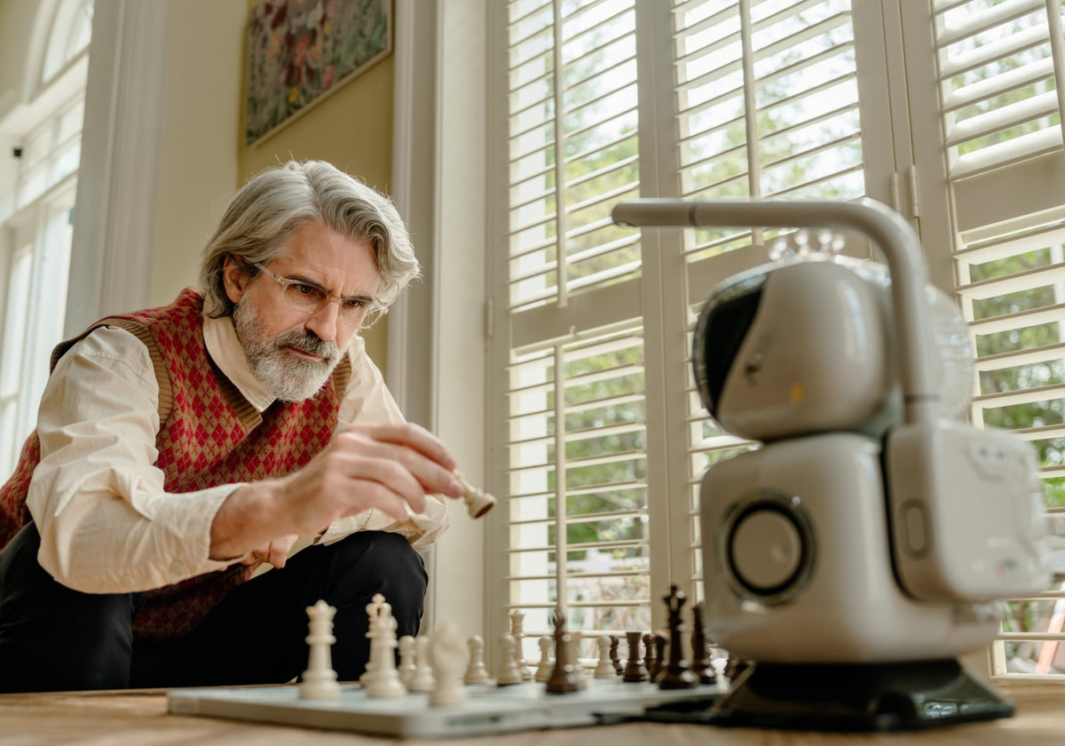 An older man moving a chess piece while playing against a SenseRobot chess robot at home.